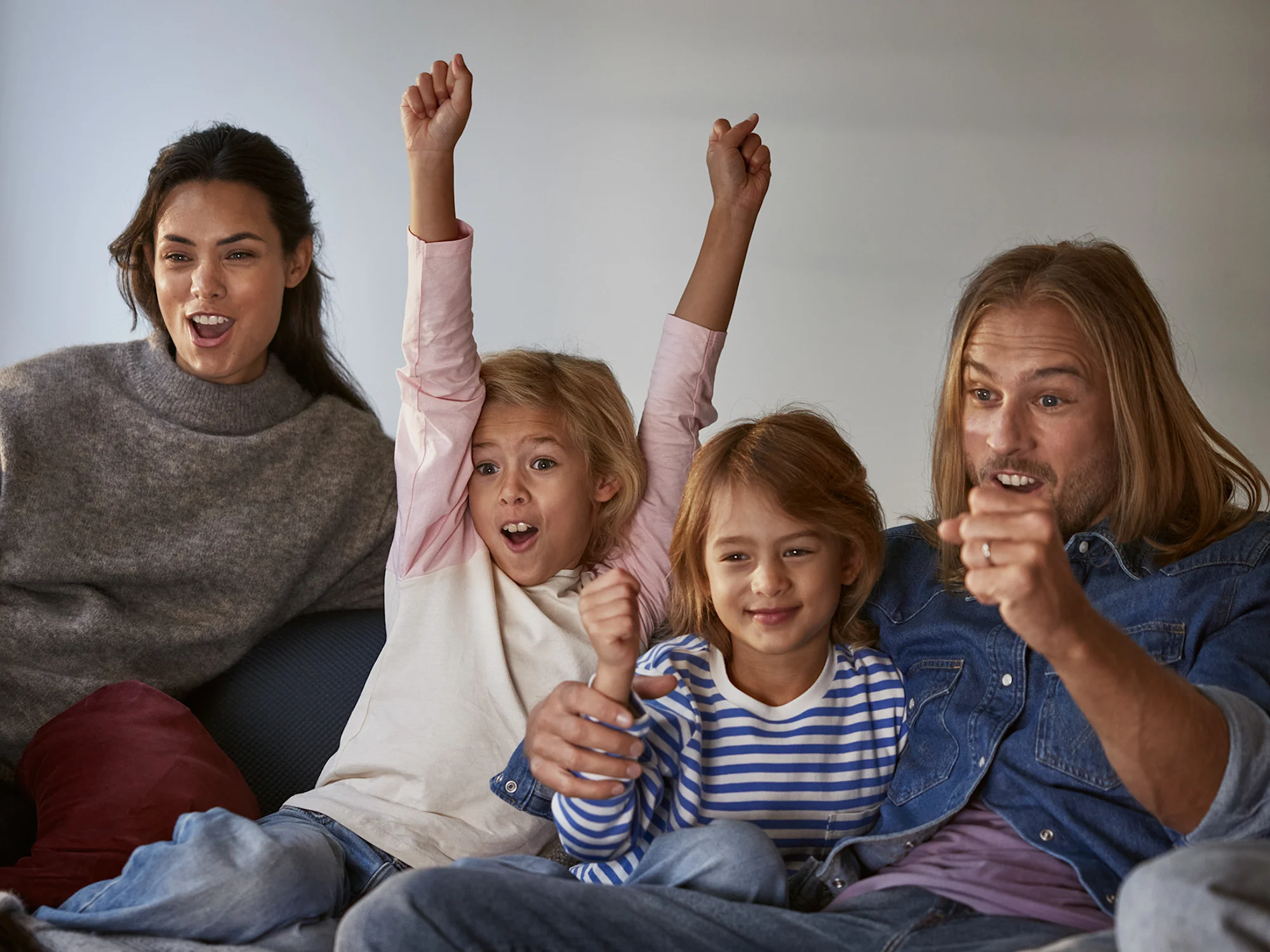 En glad familj som sitter i soffan och tittar på tv, skrattar och hejar.