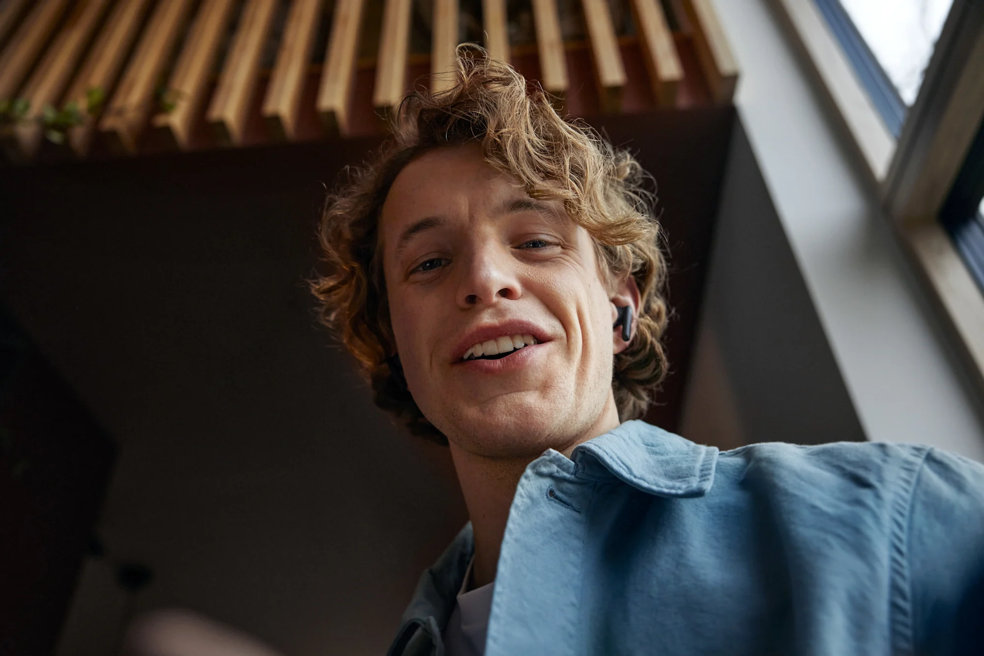 En kille med hörlurar som ler och tittar ner på sin mobil