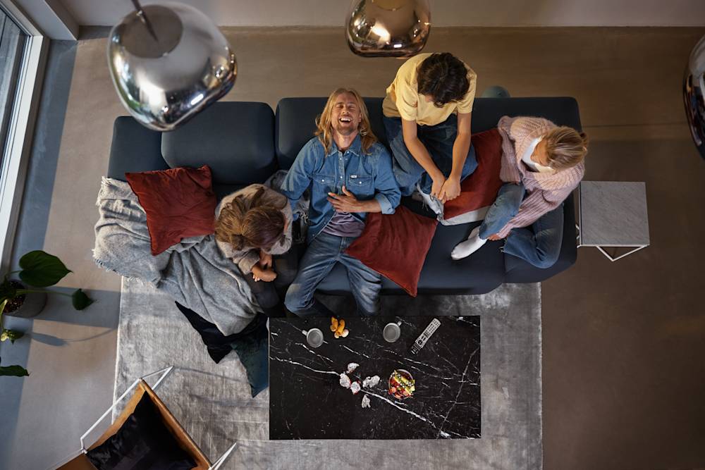 Vänner tittar på tv tillsammans i soffan och en viker sig av skratt. Streama massor av underhållning du också, med något av våra bästa streamingpaket!