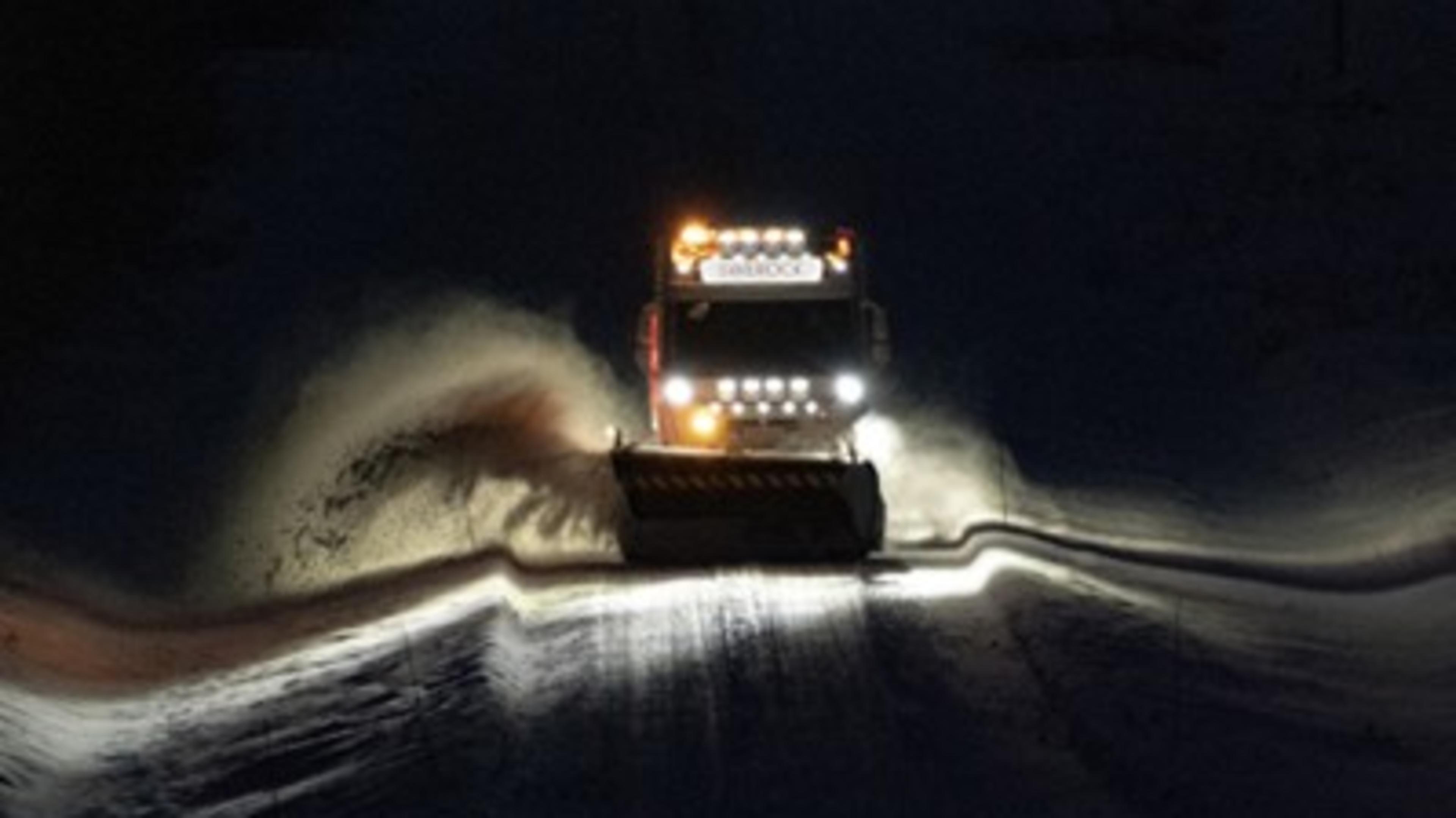 Lastbil som plogar snö från en väg i mörker