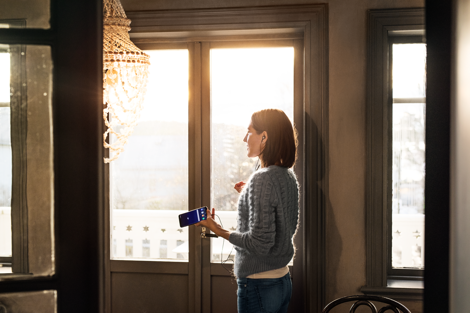 Kvinna håller telefon i handen och pratar med hörlurar.