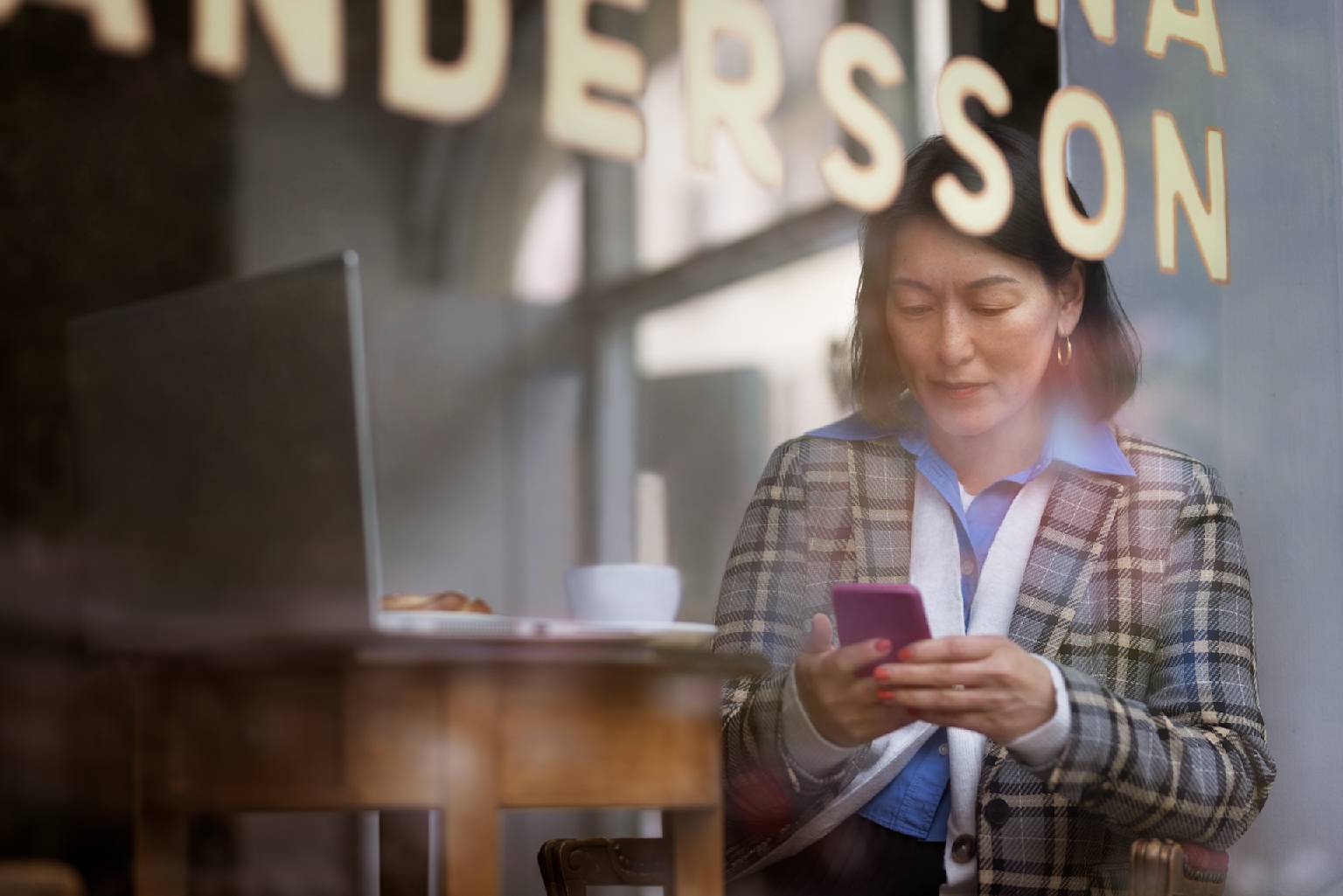 Mörkhårig kvinna med arbetar på cafe med mobil och laptop.