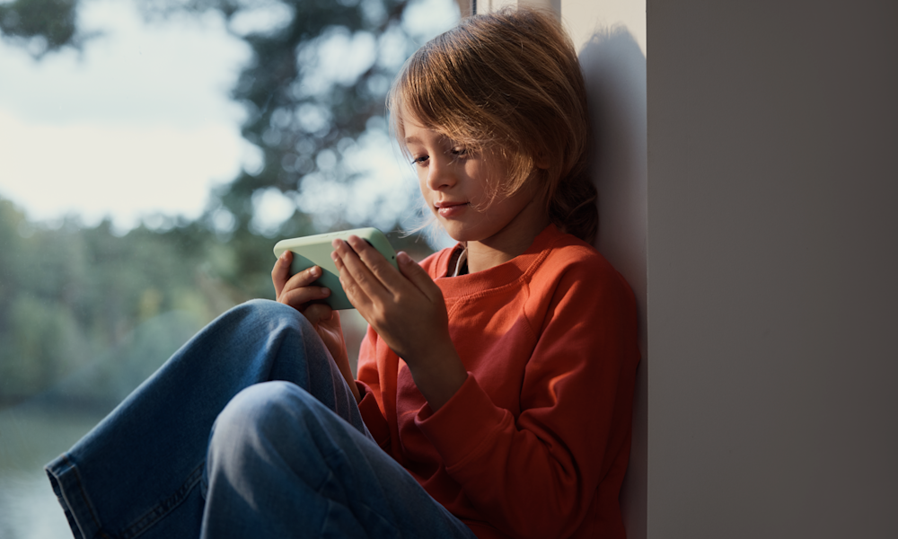 Barn sitter i fönstret och tittar på en mobiltelefon.