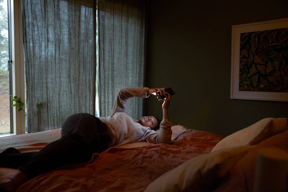 En tjej ligger i en säng och tittar på sin mobil.