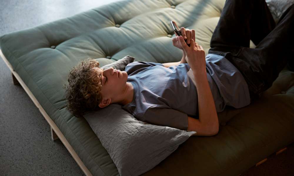 Ung kille ligger och tittar på mobilen.