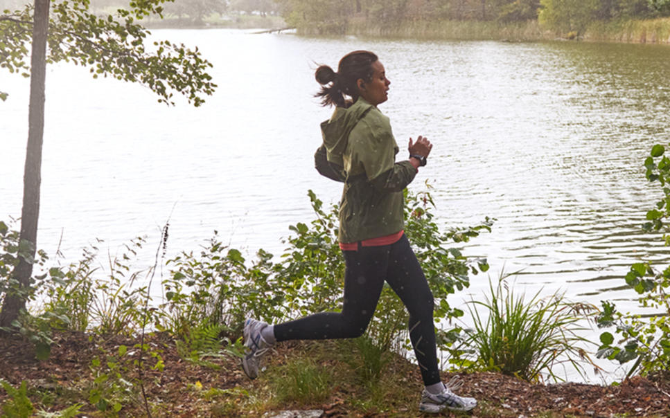 Kvinna joggar i skogen framför sjö.