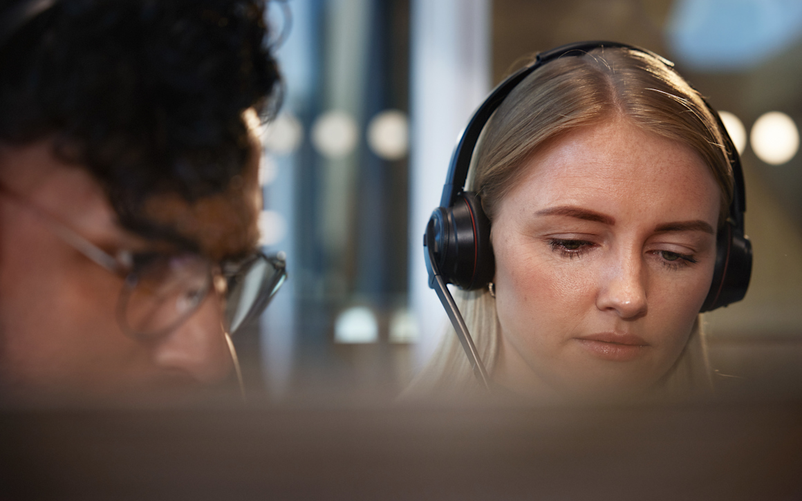 Kvinna med headset som tittar in i dator.