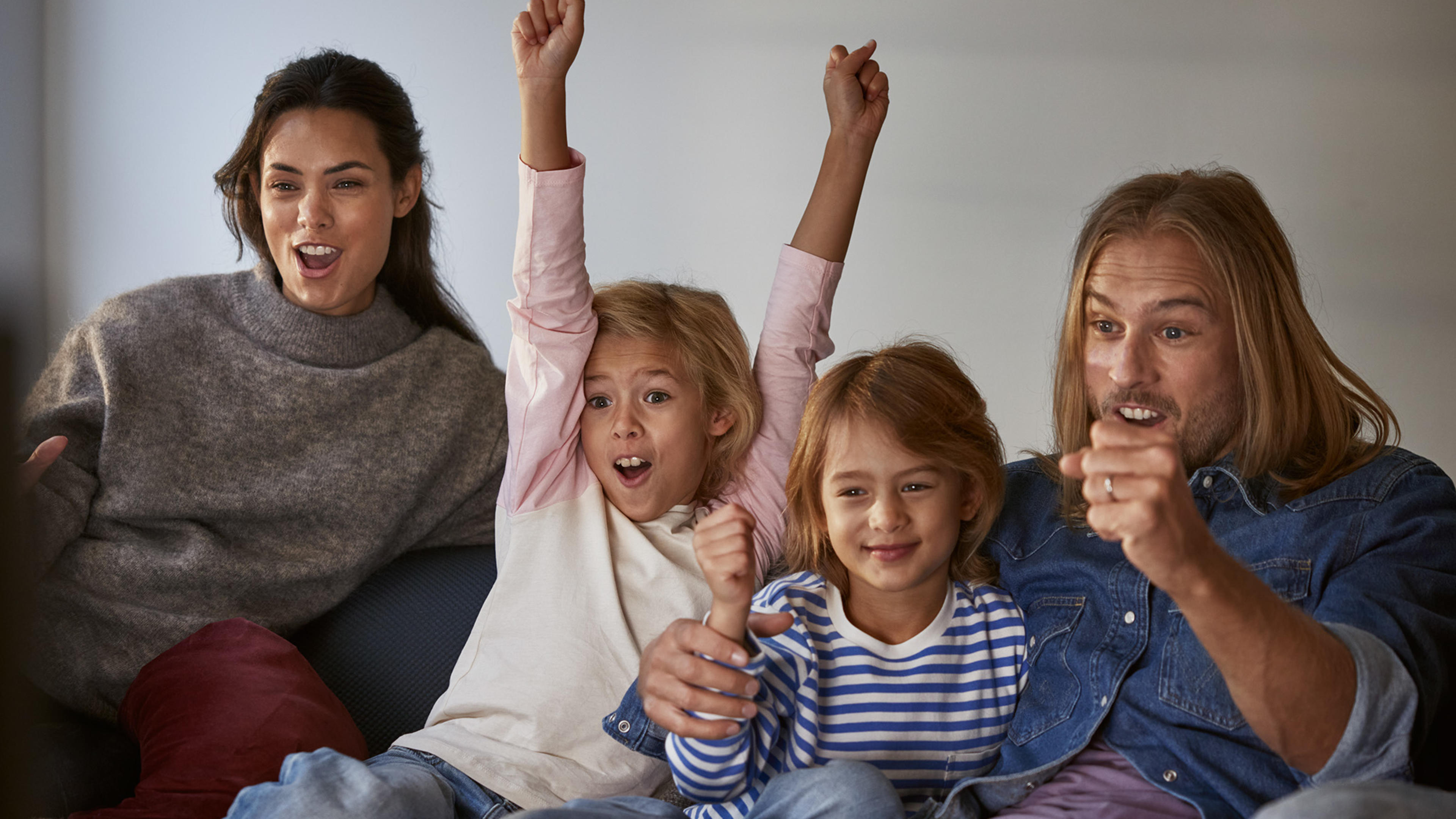 Familj med mamma, pappa och två barn sitter framför tv:n och hejar på sitt lag. Upptäck tv och streaming från Telia.