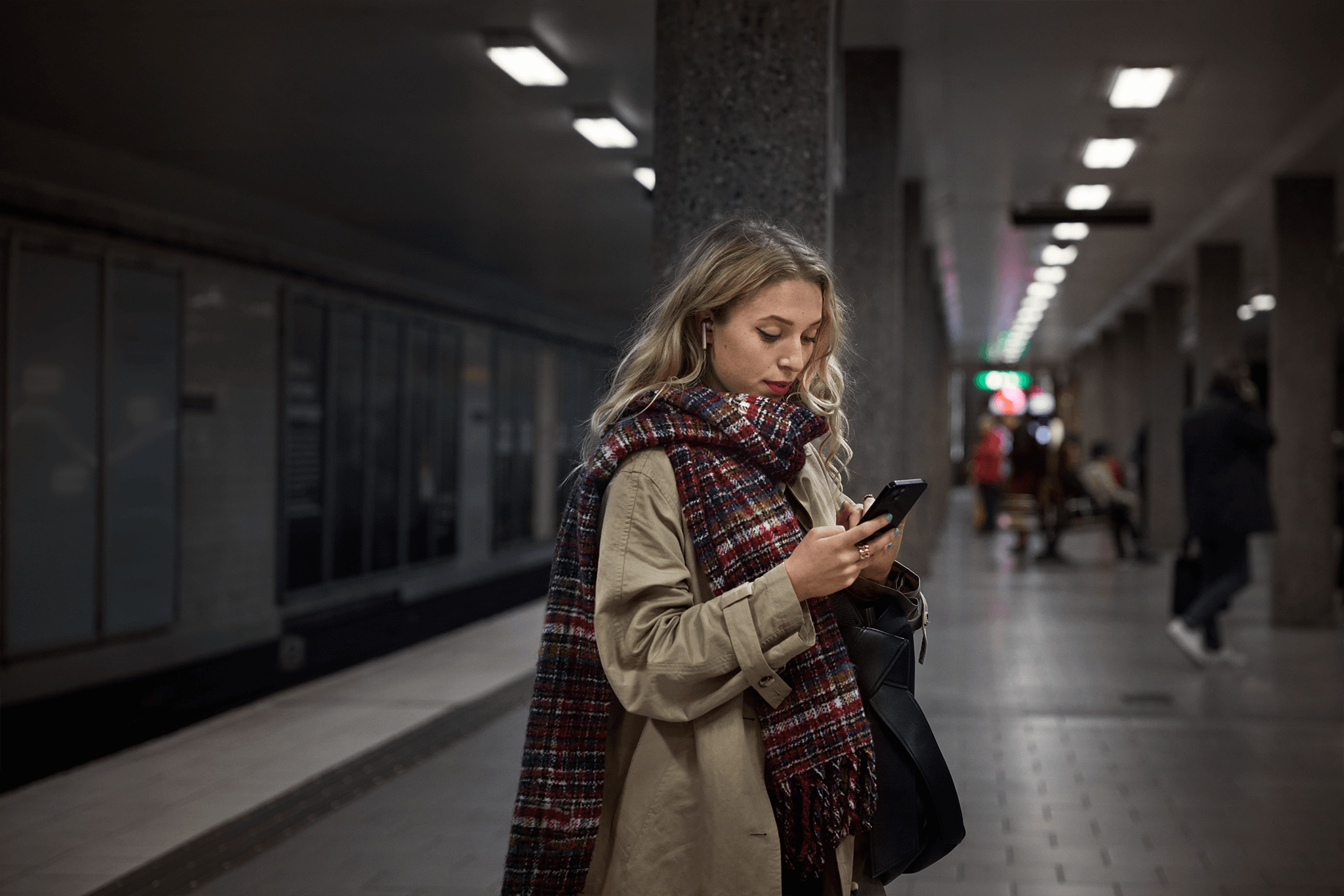 Tjej som står och surfar på sin mobil på en tunnelbaneperrong.