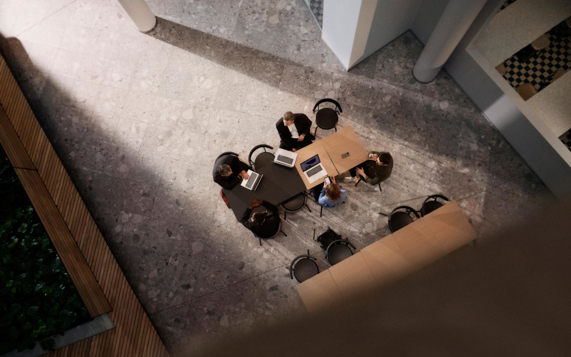 Konferensbord med arbetande människor och datorer sett ovanifrån.