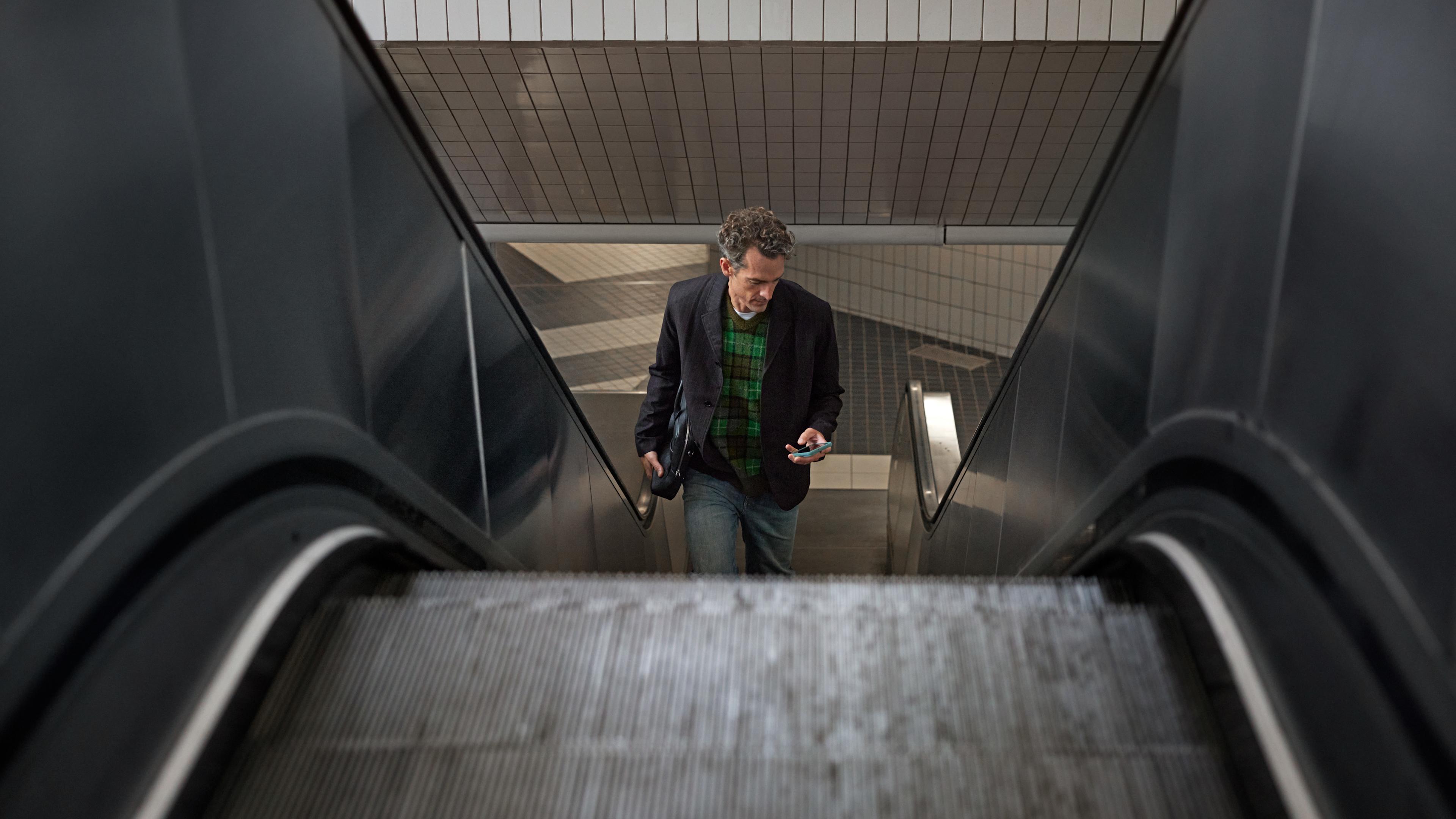 Man som åker rulltrappa och tittar på sin telefon.