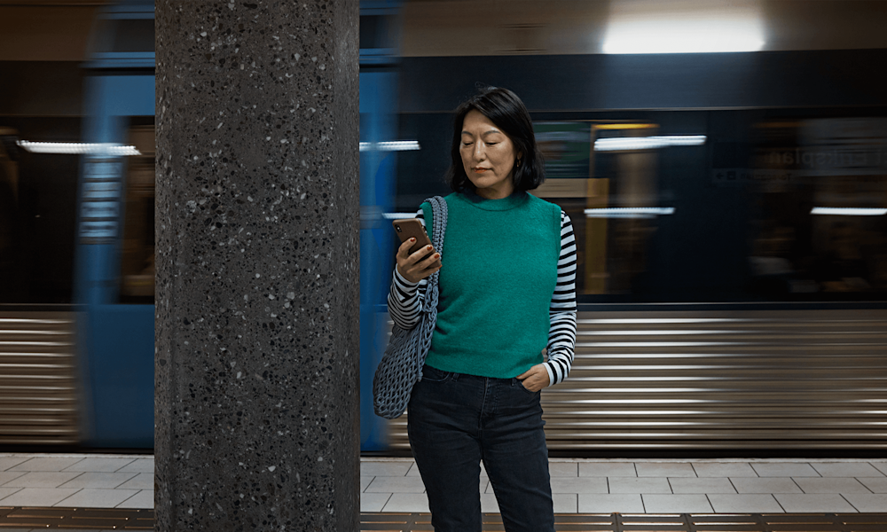 Kvinna som står och kollar på sin mobil på en tunnelbaneperrong.