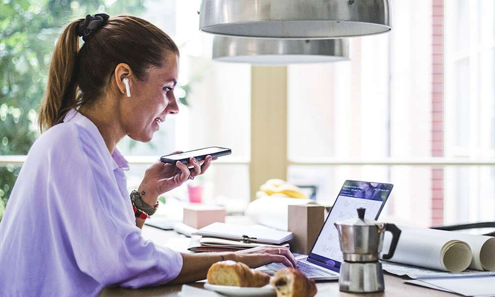 Kvinna med mobiltelefon arbetar vid laptop.