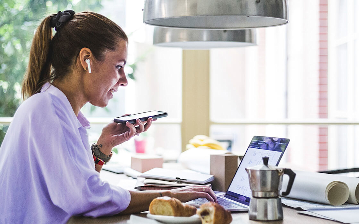 Kvinna med mobiltelefon arbetar vid laptop.