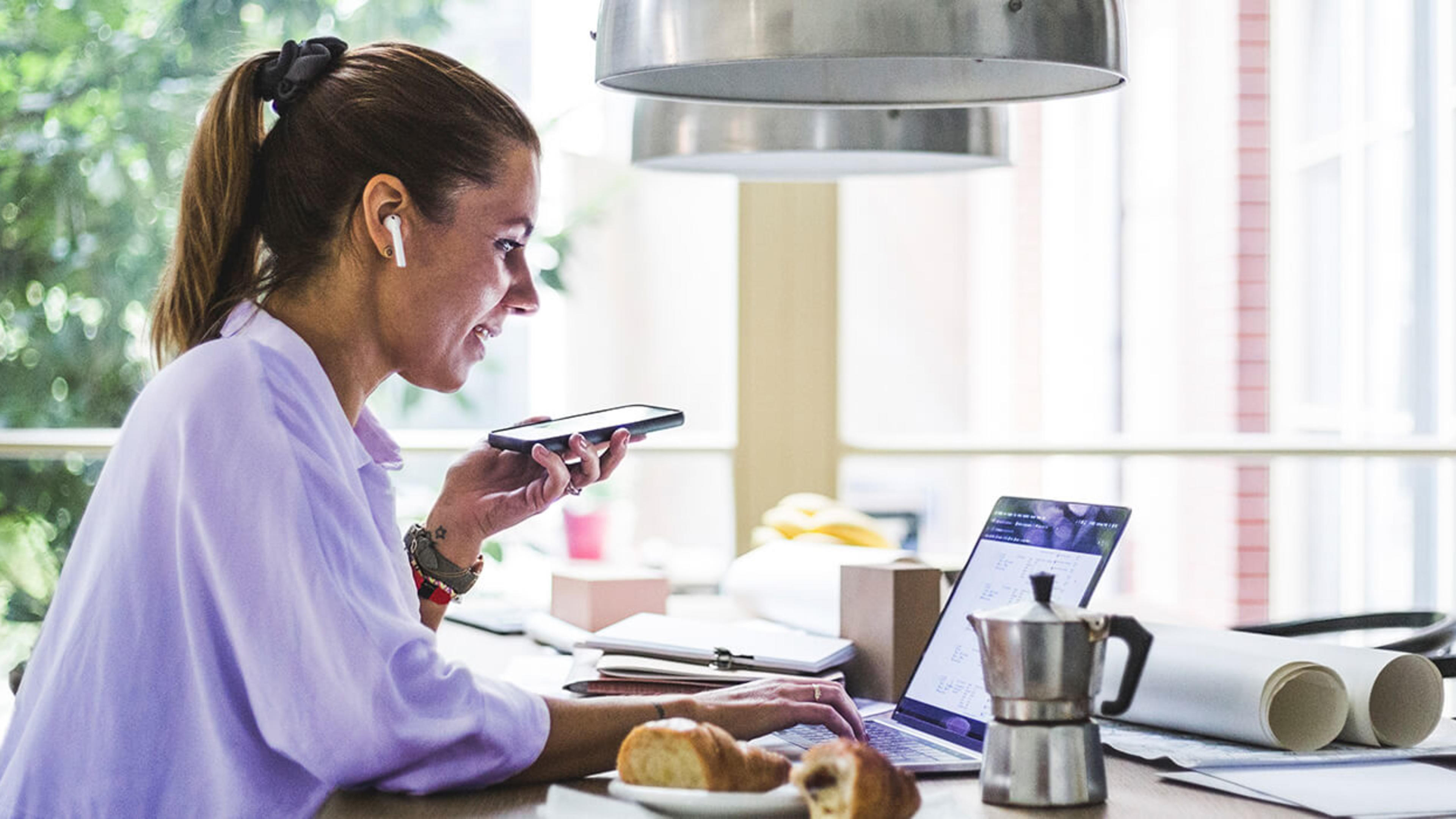 Kvinna med mobiltelefon arbetar vid laptop.