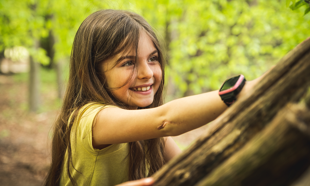 Flicka med Xplora X5-klocka leker i skogen.