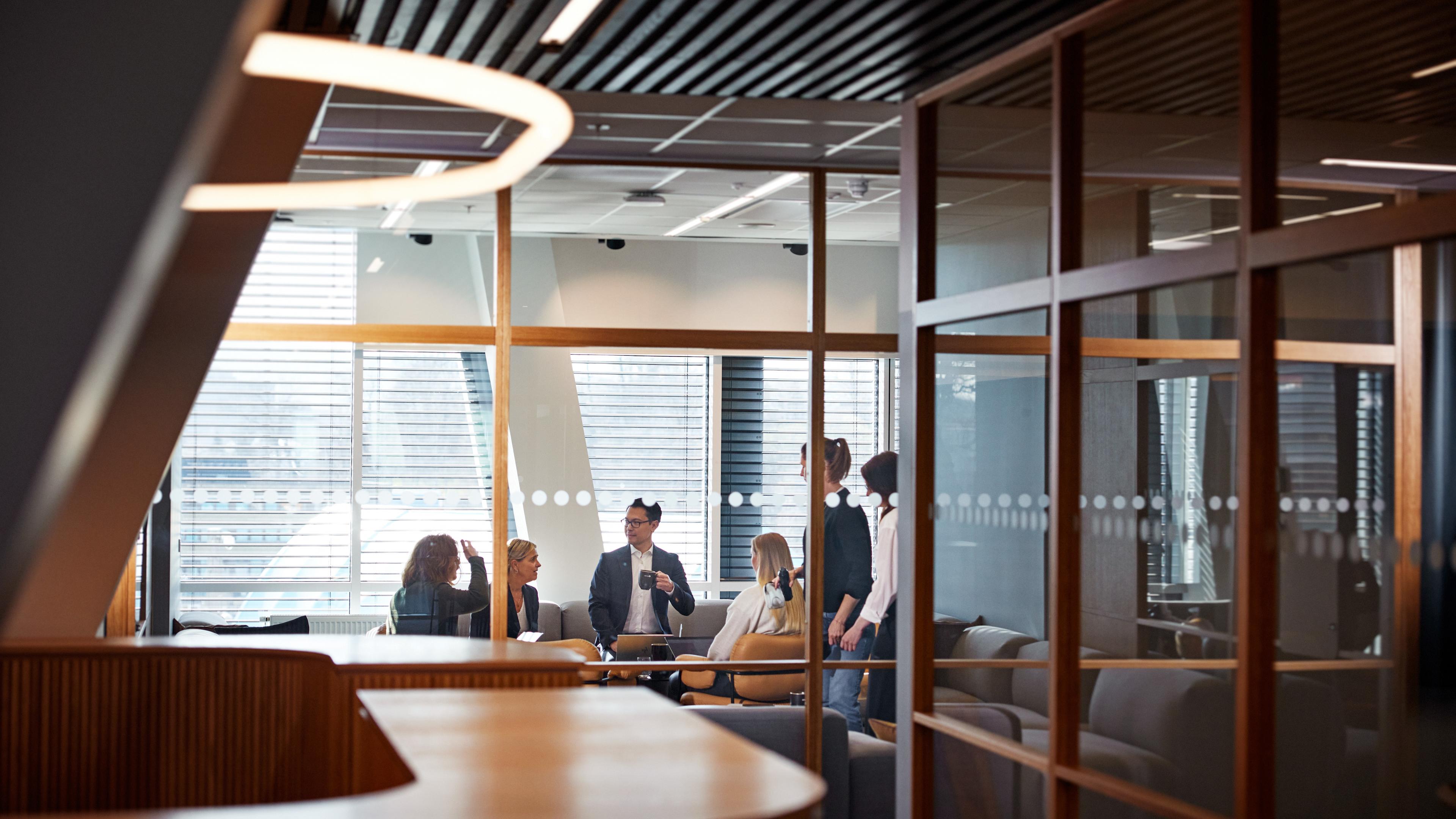 Personer som samtalar bakom glasvägg i ett konferensrum.