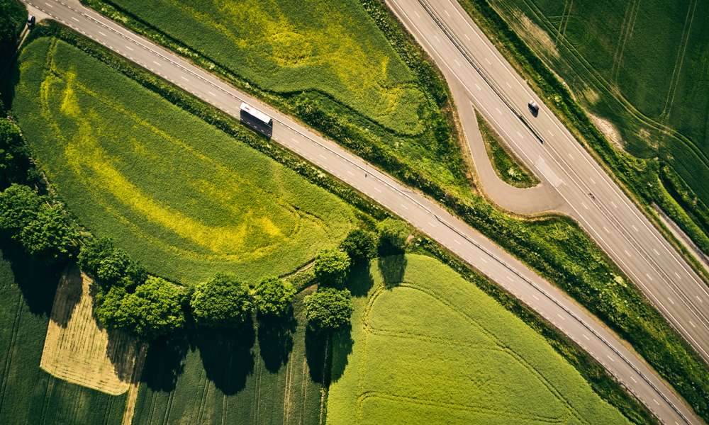 Flygfoto över väg med bil på och gröna omgivningar