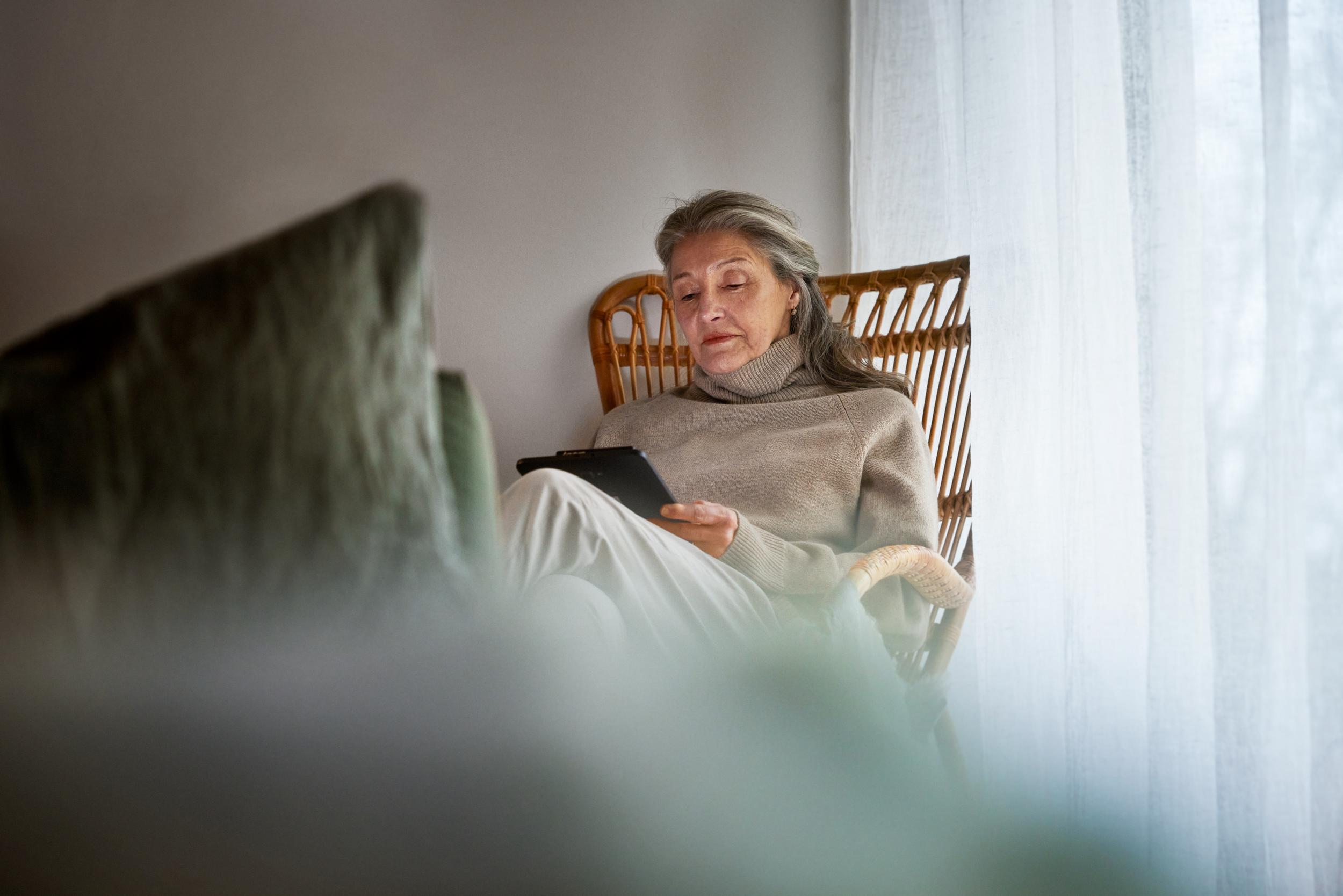 En äldre kvinna som sitter i fåtölj me surfplatta