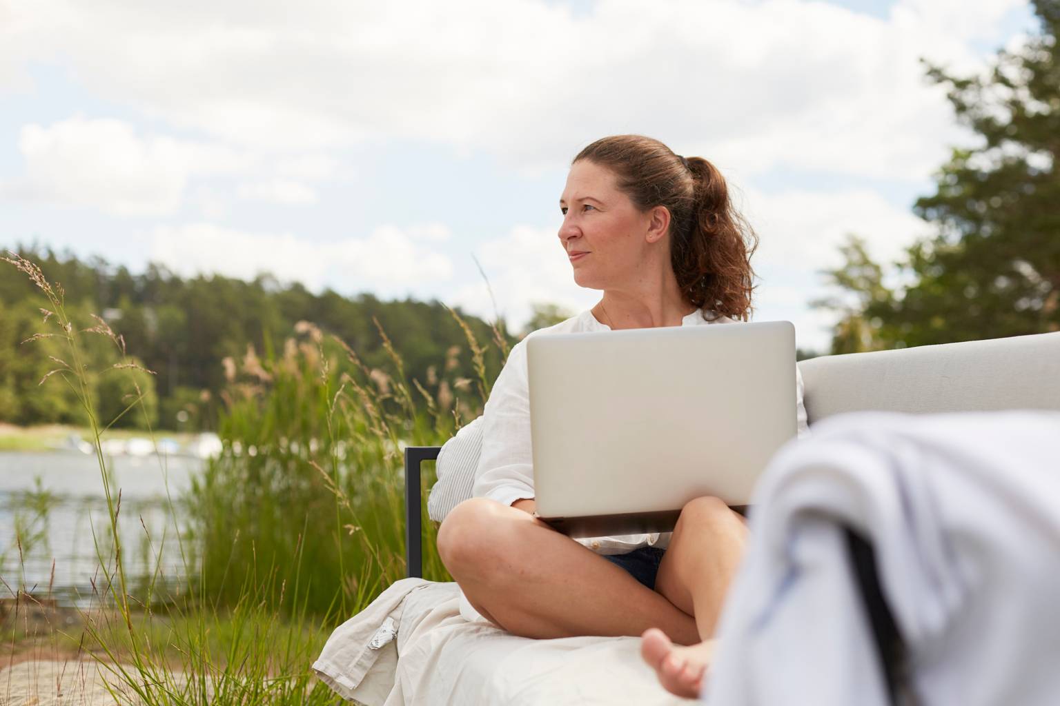 Kvinna jobbar på laptop vid sjö på sommaren