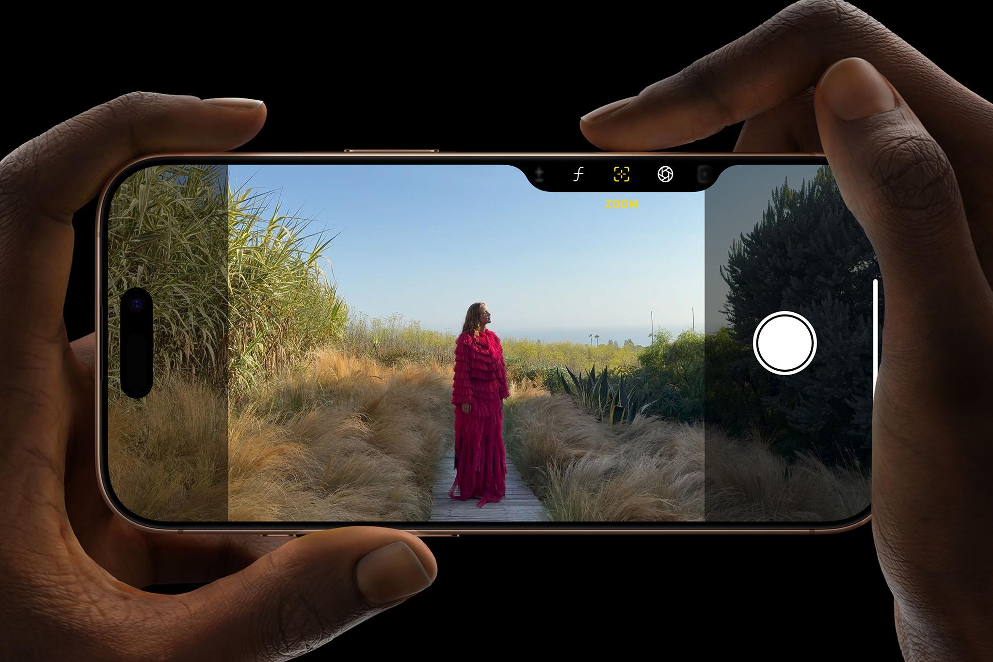 Händer som håller i en iPhone 16 och trycker på knappen för kamerareglaget med texten "Take total Camera Control" ovanför. 