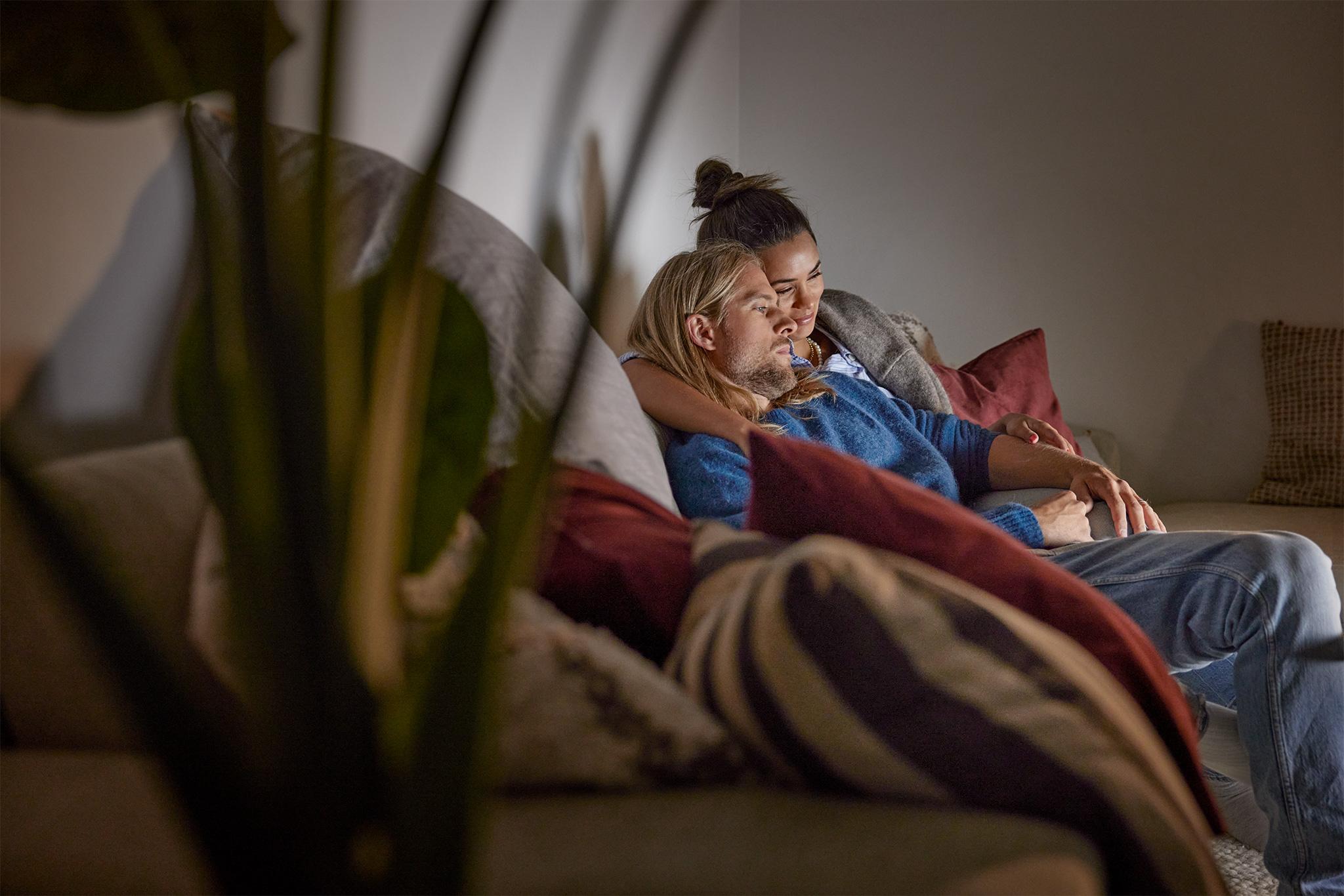 Ett yngre par sitter tillsammans i soffan och tittar på tv.