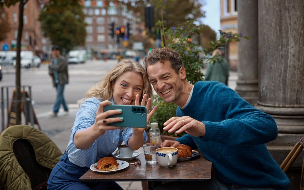Kvinna och man sitter på en uteservering och tar en selfie tillsammans och ler