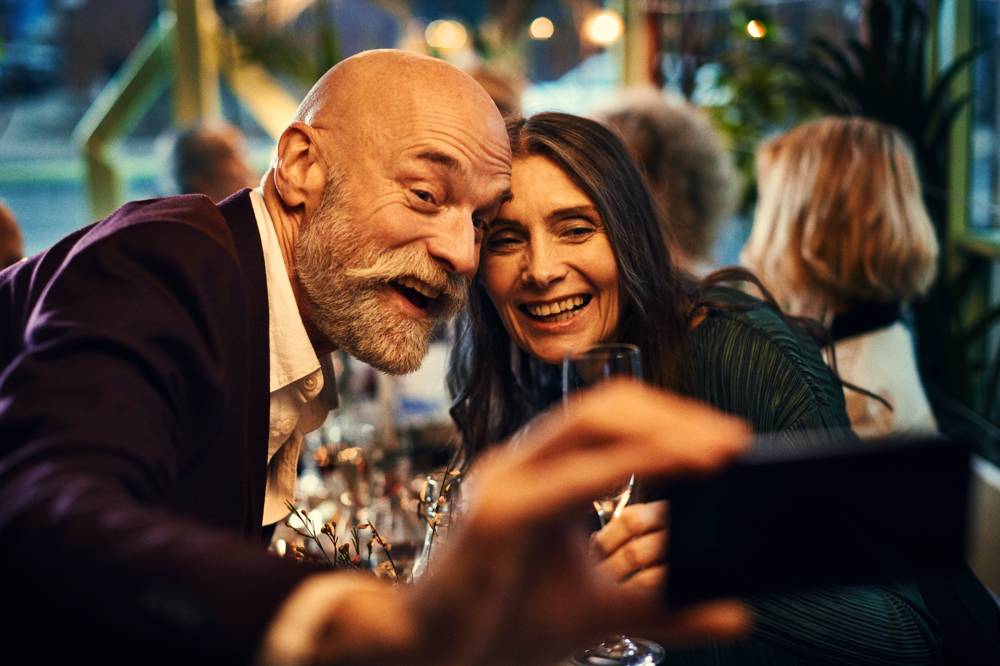 Äldre man och kvinna tar selfie i restaurangmiljö.